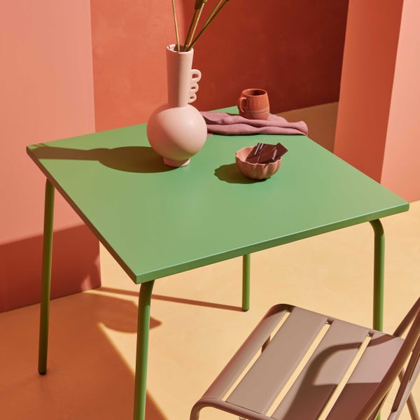 Quadratischer Gartentisch aus grünem Metall mit passendem braunem Gartenstuhl in einer hellen, minimalistischen Umgebung.