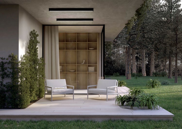 Moderne Terrasse mit hellen Loungesesseln, Bodenplatten aus Stein, linearer Deckenbeleuchtung und Blick auf Garten und Bäume.
