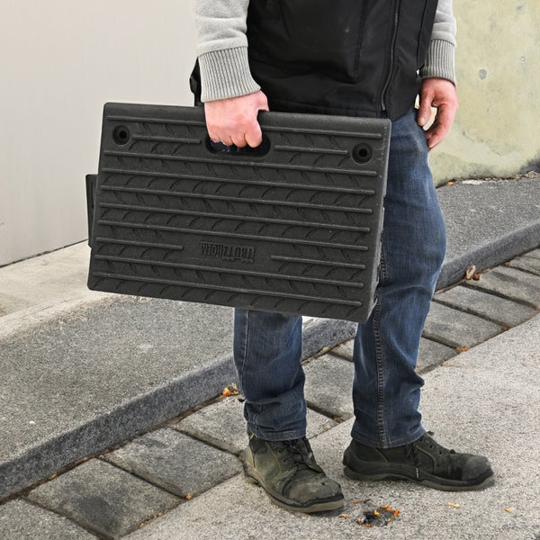 Eine Person trägt eine schwarze, tragbare Rampe mit Griff und rutschfestem Profil der Marke Trutzholm.