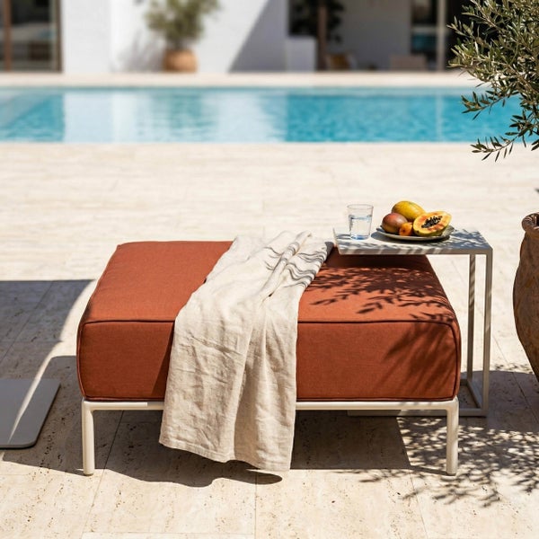 Quadratischer Gartenhocker mit Metallgestell und Polsterauflage auf einer Terrasse am Pool mit Decke und Beistelltisch.