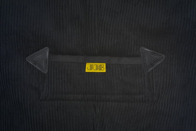 Detail einer schwarzen Cordtasche mit dreieckigen Lederverstärkungen und JOB Logo.