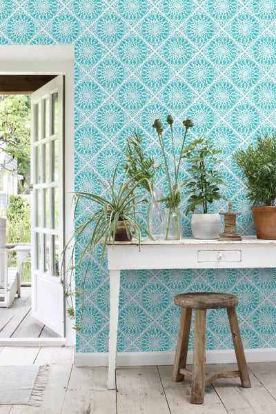 Dekoratives Zimmer mit gemusterten Tapeten, Tisch, Pflanzen und Hocker.