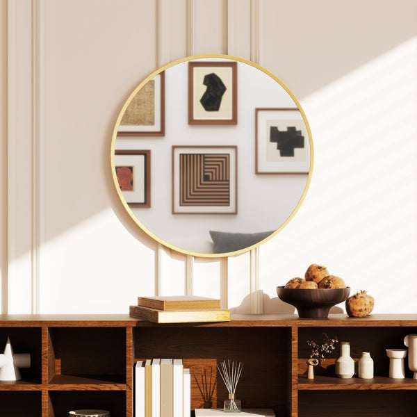 Runder Wandspiegel mit goldenem Rahmen über einem hölzernen Sideboard in einem hellen Raum mit Wandleisten.