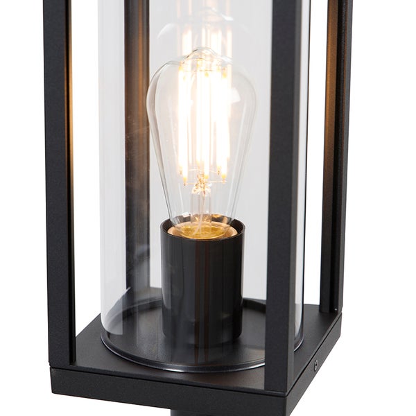 Moderne schwarze Außenleuchte mit klarem Glaszylinder und leuchtendem Filament-Leuchtmittel in einem rechteckigen Rahmen.