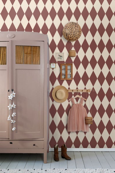 Kinderzimmer mit Rautenmuster-Tapete, Kleiderschrank und Dekorationsartikeln wie Hut, Kleid und Stiefeln.