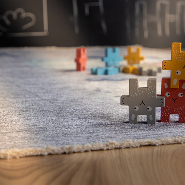 Stapelbare Holzfiguren als Hasen auf einem Kinderzimmerteppich mit Fransen und Kreidetafel im Hintergrund.
