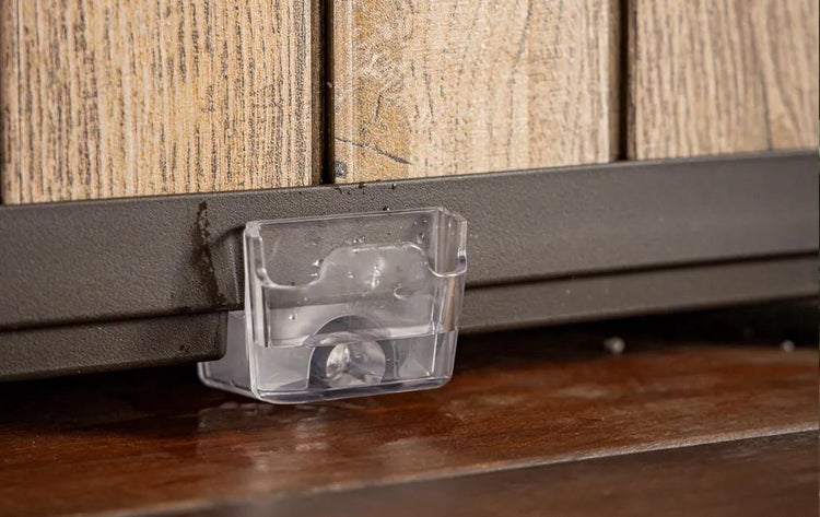 Kleiner transparenter Auffangbehälter für Wasser, montiert am Metallrahmen eines Sichtschutzzauns mit Holzoptik.