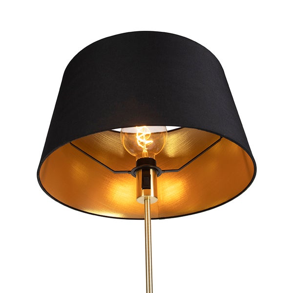 Lampe mit schwarzem Stoffschirm, goldfarbener Innenseite und eingeschaltetem Leuchtmittel.