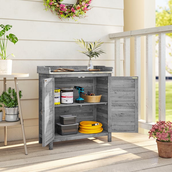 Grauer Gartenschrank aus Holz auf einem Balkon mit geöffneten Türen, gefüllt mit Gartenwerkzeug, Farbdosen und einem Schlauch.