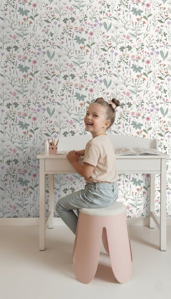 Ein Mädchen sitzt an einem Kinderschreibtisch vor einer Wand mit Blumentapete