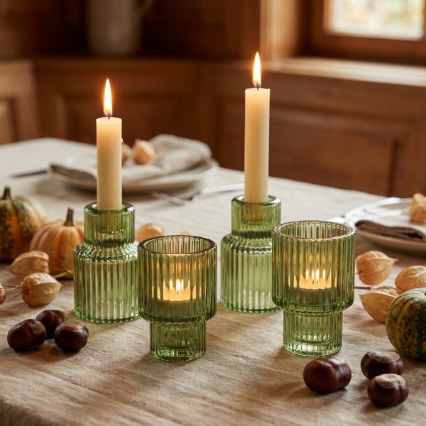 Set aus vier gerippten Glas-Kerzenhaltern in verschiedenen Formen auf einem festlich gedeckten Tisch mit Herbstdekoration wie Kastanien und Kürbissen.