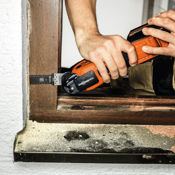 Mann schneidet mit einem oszillierenden Multifunktionswerkzeug ein Holzfenster