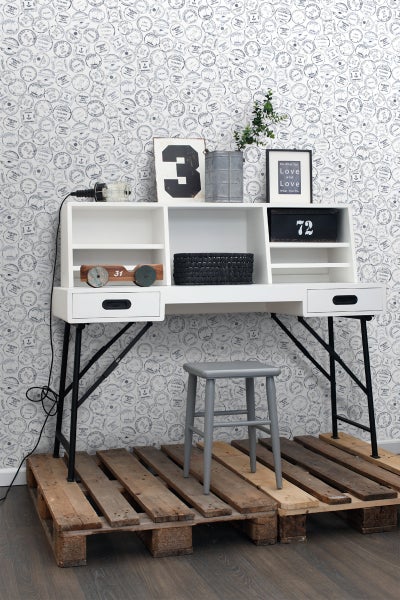 Weißer Schreibtisch mit Ablagefächern und schwarzem Metallgestell auf Holzpaletten mit grauem Hocker vor gemusterter Tapete