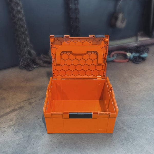 Offene orangefarbene Werkzeugbox aus Kunststoff mit Wabenstruktur im Deckel und Tragegriff.