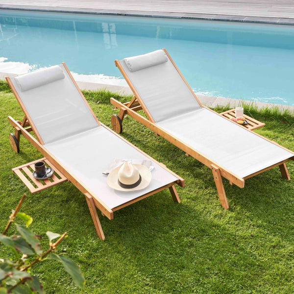 Zwei hölzerne Sonnenliegen mit hellem Textilbezug und Kopfkissen auf einer Rasenfläche neben einem Pool.