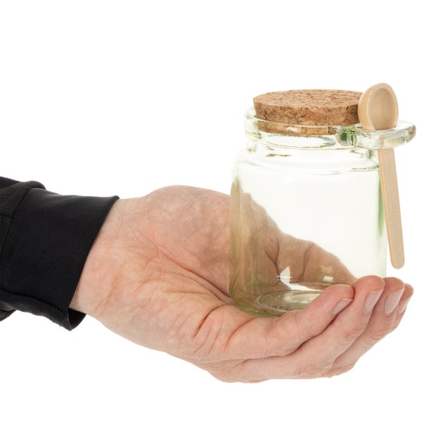 Kleines Glasgefäß mit Korkdeckel und Holzlöffel in einer Hand zur Größenansicht.
