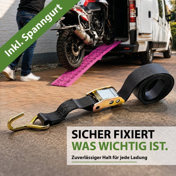 Ein Zurrgurt mit Ratsche und Haken liegt auf dem Boden, im Hintergrund verlädt eine Person ein Motorrad über eine Rampe in einen Transporter.