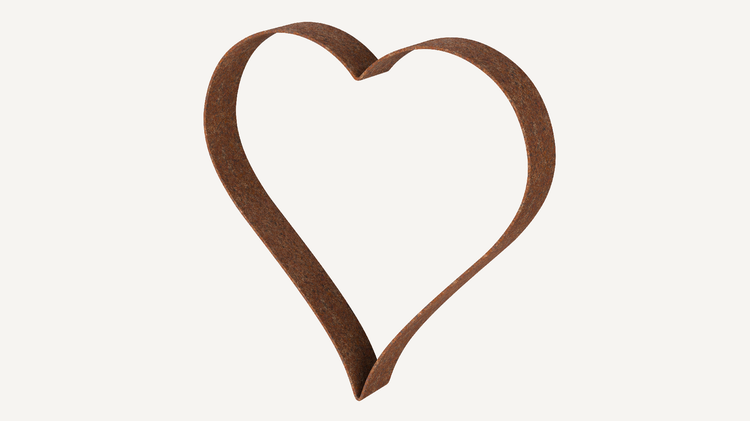 Dekoratives Herz aus Metall im Gartenbeet zwischen Pflanzen