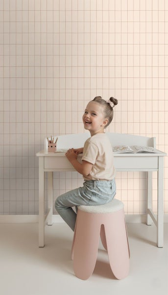 Mädchen sitzt an einem weißen Schreibtisch auf einem Hocker mit Fellbezug, im Hintergrund eine Wand mit Fliesentapete