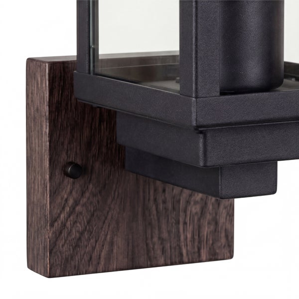 Laternenförmige Außenwandleuchte aus dunklem Metall und Glas mit einer rechteckigen Wandhalterung in dunkler Holzoptik.