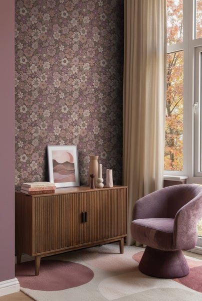 Vliestapete mit floralem Retro-Muster in einem Wohnzimmer mit Holzkommode, lila Sessel und beigen Vorhängen vor einem Fenster.