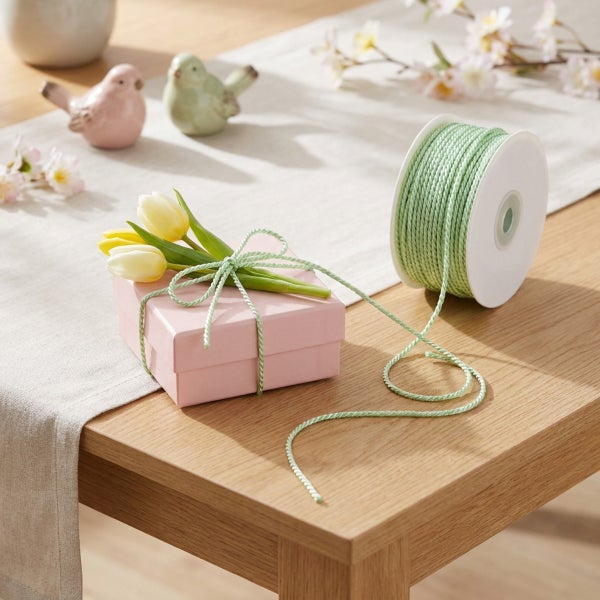 Dekorative Kordel auf einer Spule zum Verpacken von Geschenken, kombiniert mit einer Geschenkbox und Frühlingsdekoration auf einem Holztisch.