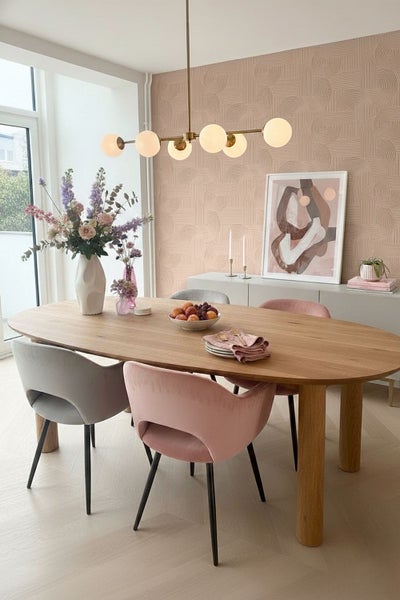 Modernes, helles Esszimmer mit ovalem Holztisch, Samtstühlen, einer goldenen Pendelleuchte mit Glaskugeln und geometrisch gemusterter Tapete.