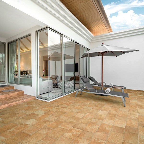 Moderne Terrasse mit Fliesenboden vor einer bodentiefen Glasfront, inklusive zwei Sonnenliegen und einem Sonnenschirm.