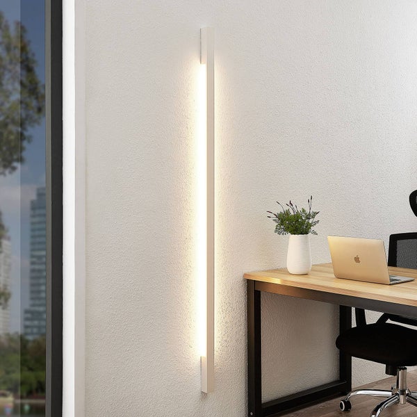 Moderne vertikale LED-Wandleuchte mit warmweißem Licht in einem Büro neben einem Schreibtisch.