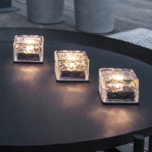 Drei dekorative Eiswürfel-Teelichthalter aus Glas auf einem Tisch.