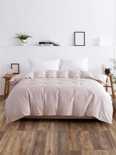 Minimalistisches Schlafzimmer mit beigem Bettbezug, weißen Kissen, Holzboden, Beistelltischen und Dekoration auf einer Wandleiste.