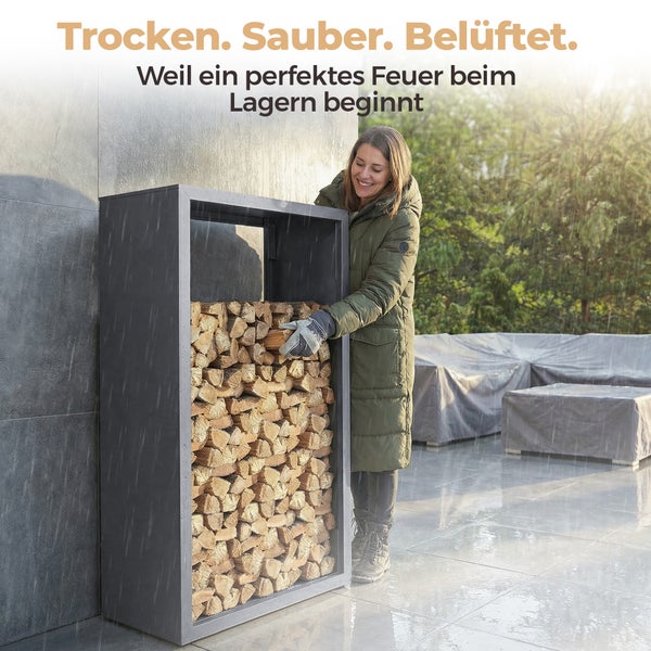 Eine Frau stapelt Brennholz in ein Kaminholzregal aus Metall auf einer regnerischen Terrasse.