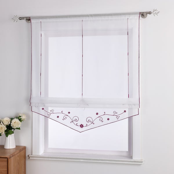 Gardine mit floralem Muster am unteren Rand vor einem Fenster.
