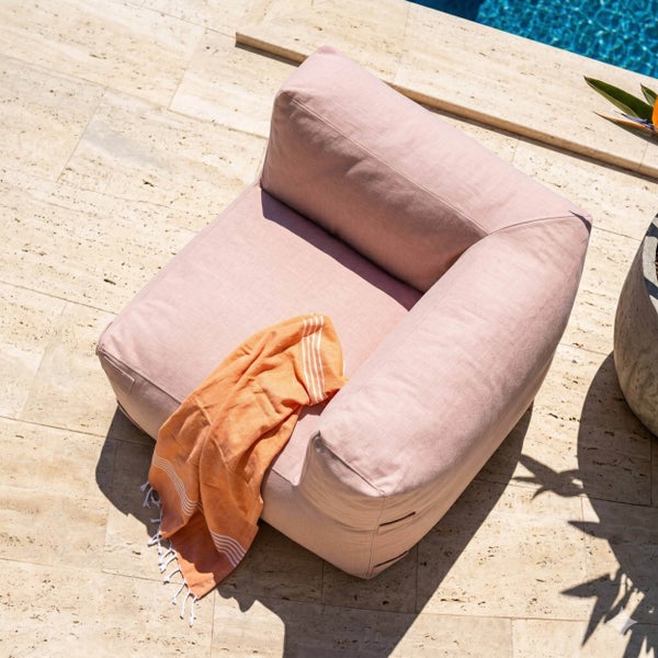 Rosa Outdoor-Loungesessel aus Stoff mit orangefarbenem Handtuch auf einer Steinterrasse am Pool.