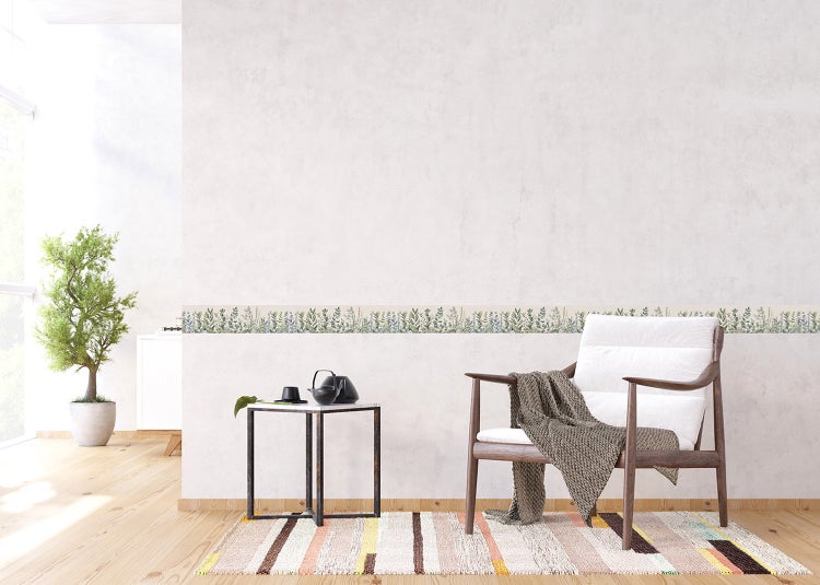 Tapetenbordüre mit Pflanzenmotiv an einer hellen Wand in einem hellen Wohnzimmer mit Sessel, Beistelltisch und Teppich.