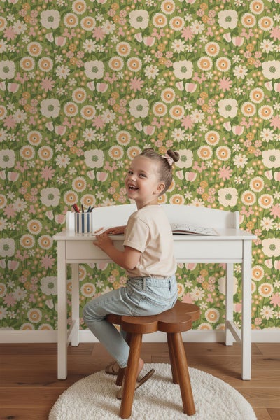 Vliestapete mit Blumenmuster im Retrostil an der Wand eines hellen Kinderzimmers hinter einem Schreibtisch und einem Holzhocker.