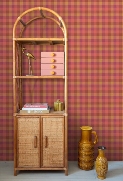 Karierte Tapete mit einem Muster aus roten und orangenen Quadraten in einem Raum mit einem Rattan-Regal und Dekorationsartikeln.