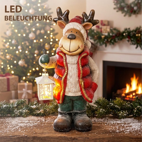 Dekorative Rentierfigur mit LED Beleuchtung in winterlicher Kleidung und Laterne vor einem Kamin und Weihnachtsbaum.