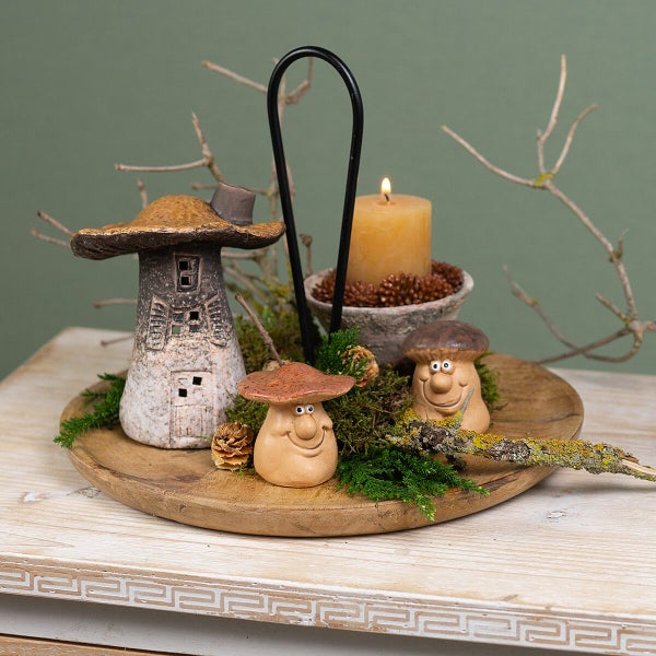 Herbstliche Tischdekoration mit Pilzhaus aus Keramik, zwei Pilzfiguren, brennender Kerze auf einem Holztablett mit Moos und Zweigen.
