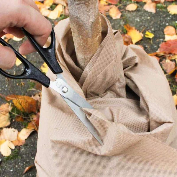 Eine Person schneidet mit einer Schere eine Baumschutzhülle aus Stoff