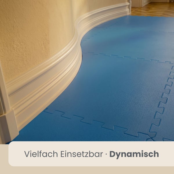 Blaue Bodenschutzmatte aus Schaumstoff mit Puzzlerand, verlegt in einem Raum entlang einer geschwungenen Wand mit weißer Sockelleiste.