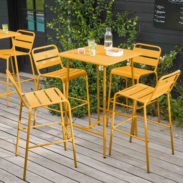 Gelbe Bar-Gartengarnitur aus Metall bestehend aus einem quadratischen Stehtisch und vier Barhockern auf einer Holzterrasse.
