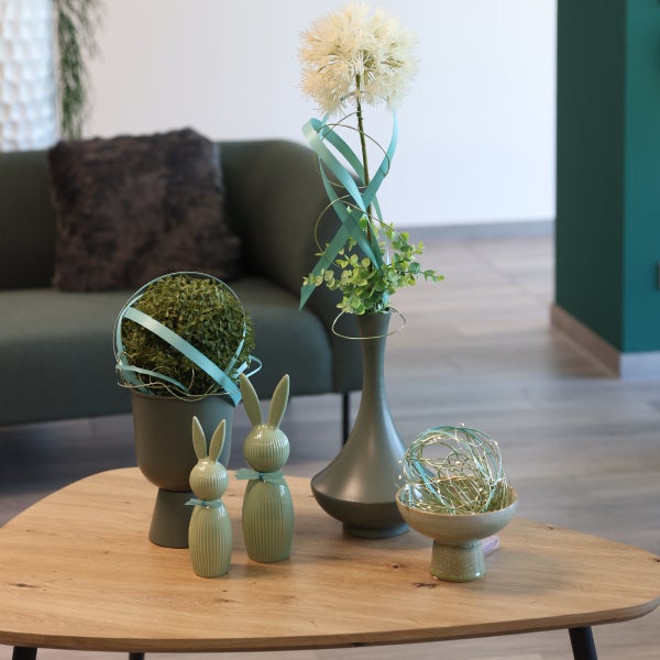 Dekorative Szene mit Osterhasenfiguren, Pflanzen und einer Lichterkette auf einem Tisch