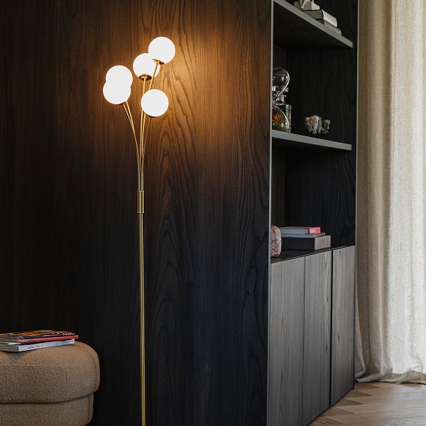 Stehlampe mit fünf Leuchtkörpern aus Glas neben dunklem Holzschrank