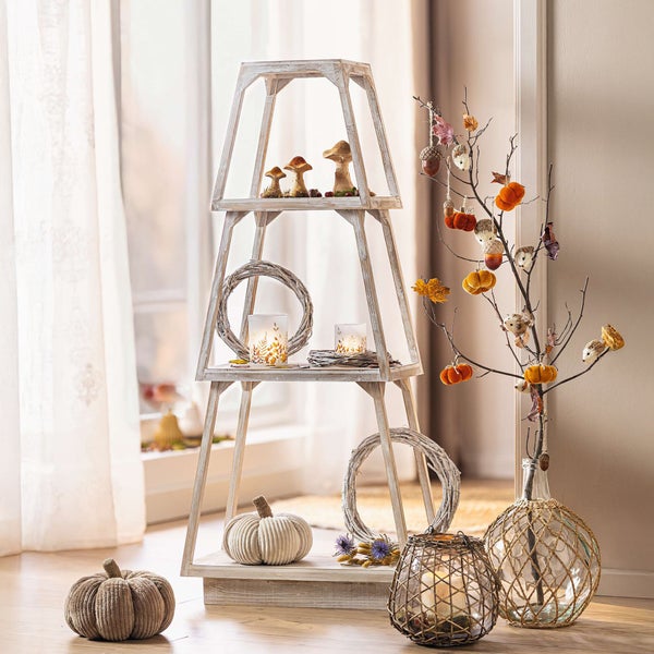 Herbstliche Dekoration mit Holzregal, Pilzfiguren, Kränzen, Kerzenhaltern und Kürbissen.
