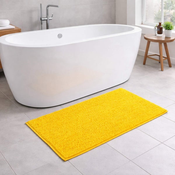 Gelber Badteppich vor einer freistehenden weißen Badewanne auf grauen Fliesen in einem hellen Badezimmer.