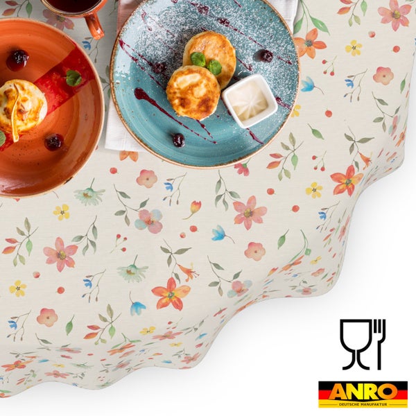 Abwischbare Tischdecke mit Blumenmuster, dekoriert mit Tellern, Lebensmittelkontaktzeichen und ANRO DEUTSCHE MANUFAKTUR Logo.