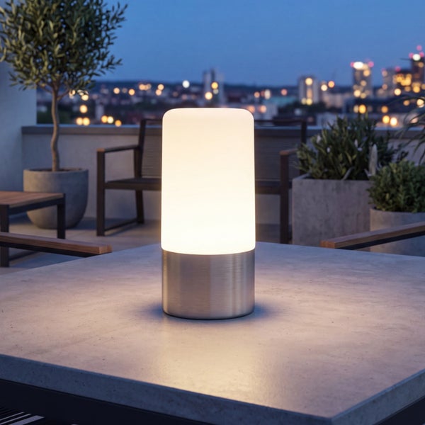 Zylindrische LED Tischleuchte für den Außenbereich mit Metallsockel und mattem Leuchtschirm auf einem Tisch vor städtischer Kulisse.