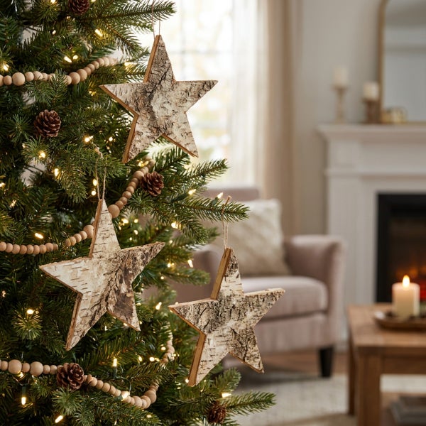 Drei Weihnachtsstern Anhänger aus Birkenholz an einem Weihnachtsbaum mit Lichterkette, Tannenzapfen und Holzperlenkette.