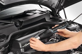Person verwendet ein Heißluftgebläse für Arbeiten im Motorraum eines Autos.